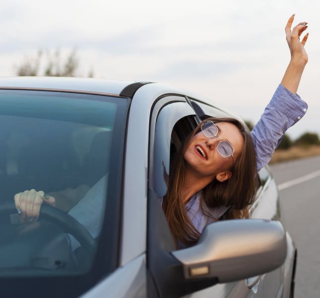 Mulher sorrindo dentro de um carro em dia ensolarado.